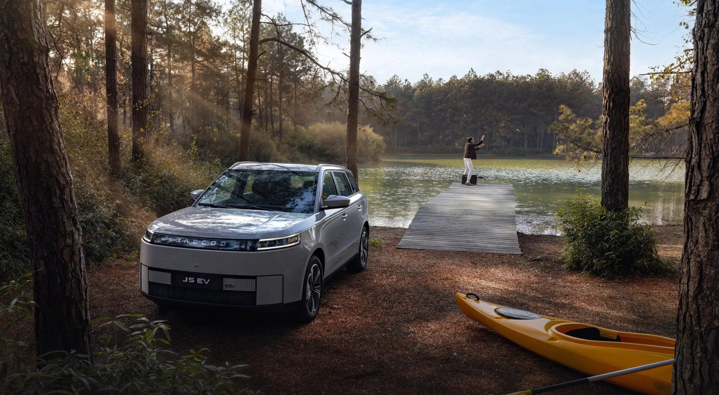 Jaecoo J5 EV parked by a forest lake with kayaks